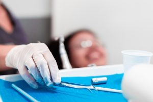 Dentist in white gloves holding dental instruments over blue tray during professional cleaning procedure.