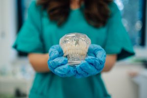 Dental professional holding clear tooth model wearing blue gloves in Ruidoso dental practice.