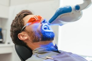 Patient receiving professional teeth whitening treatment with blue LED light technology.