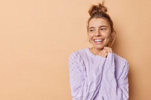 Happy patient in lavender sweater smiling after tooth whitening treatment.