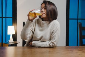 Woman drinking beer after tooth extraction, demonstrating post-extraction alcohol consumption risks.