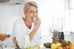 Smiling woman eating fresh fruit during root canal recovery in a bright kitchen.