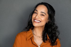 Smiling woman in orange shirt with healthy white teeth demonstrating cosmetic dental results.
