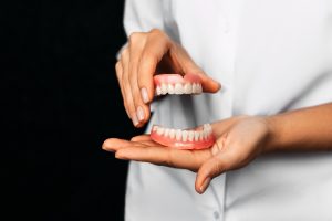 Dentist holding upper and lower dentures to demonstrate proper fit and care for denture maintenance.