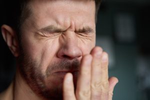 Man with closed eyes touching his face, experiencing discomfort from bad breath or dental issues.
