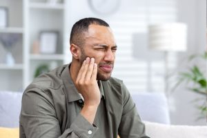 Man holding his cheek in pain, illustrating sensitive tooth discomfort and the need for dental relief.