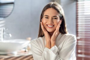 Smiling woman with bright white teeth in dental office bathroom setting.