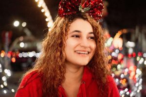 Happy woman with bright smile wearing red holiday sweater and festive bow in Ruidoso.