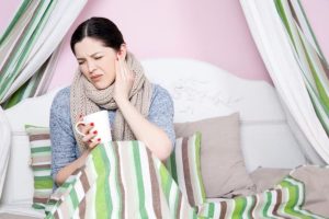 Woman with sensitive tooth pain holding her cheek while wrapped in a blanket at home.