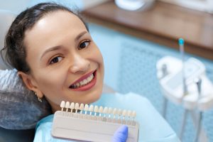 Woman holding a dental shade guide showing tooth color options for veneers.