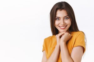 Woman in yellow shirt smiling brightly, representing a healthy white smile after dental whitening treatment.