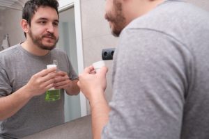 Man applying mouthwash in bathroom mirror for treating lie bumps on tongue.