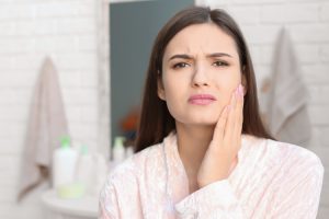 Woman experiencing dental pain, touching her cheek in a bathroom setting.