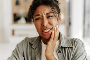 Woman holding her cheek in pain, experiencing jaw discomfort after dental treatment.