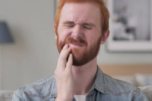 Man with red beard experiencing tooth pain, holding his cheek in discomfort.