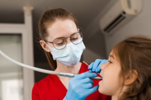 Dentist examining child patient's teeth during dental checkup in office.