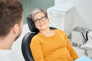 Female dentist in yellow shirt smiling with patient during consultation at dental office.