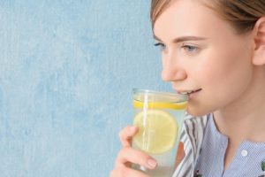 Young person drinking lemon water against blue background for teeth whitening discussion.
