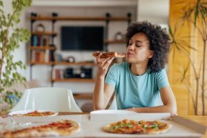 Woman eating pizza at home, experiencing metallic taste after dental implants.
