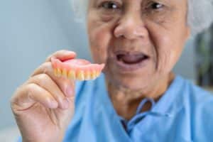 Dentist holding a full upper denture to demonstrate proper fit and appearance for new denture wearers.